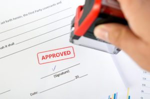 A person is holding a red rubber stamp on top of papers.