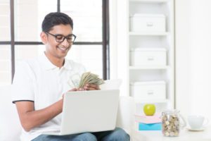 A man sitting in front of a laptop holding money.